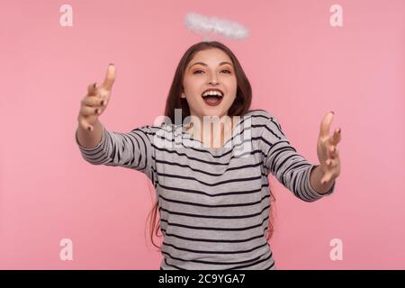 Ritratto di donna ospitale angelica con nimbus santo sulla testa che alza le mani per abbracciare e accogliere l'ospite con un sorriso toothy, felice di incontrarsi Foto Stock