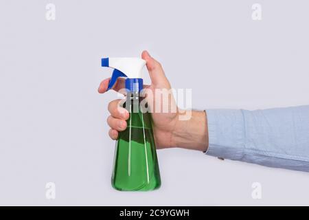 Mano maschio che tiene il flacone spray verde su sfondo bianco. Primo piano della pistola a spruzzo Foto Stock