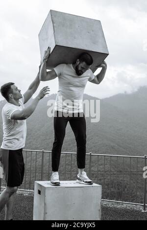 L'allenatore professionale di crossfit aiuta l'atleta a eseguire squadre con blocchi di peso, allenamenti all'aperto su sfondo di natura montana. Foto Stock