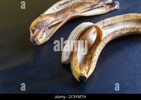 Foto dettagliata scartata buccia di banana su sfondo nero. La buccia di banane sopramature con macchie marroni. Rifiuti alimentari. Primo piano. Messa a fuoco selettiva. Foto Stock
