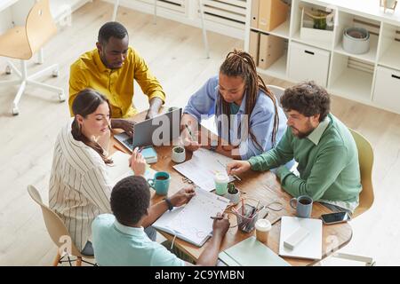 Vista ad alto angolo del team creativo contemporaneo che lavora insieme a un tavolo ordinato con tazze e oggetti fissi, lavoro di squadra o studio di concetto, spazio di copia Foto Stock