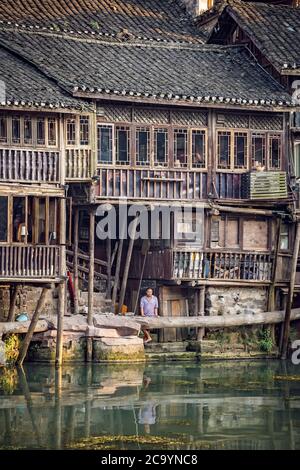 Feng Huang, Cina - Agosto 2019 : uomo cinese di mezza età che si trova nel balcone di una vecchia casa di legno storico Diaojiao sulla riva del fiume di Tuo ri Foto Stock