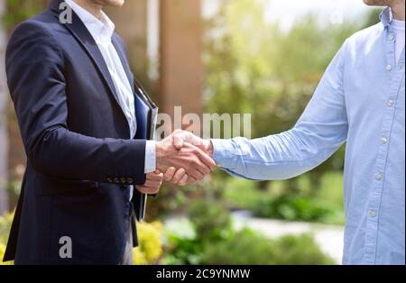 Closeup di agente immobiliare e il suo cliente scuotendo le mani vicino a nuova casa Foto Stock