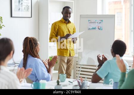 Ritratto di giovane afroamericano in piedi da lavagna in sala conferenze e sorridente con multi-etnico business team applauding, copia spazio Foto Stock