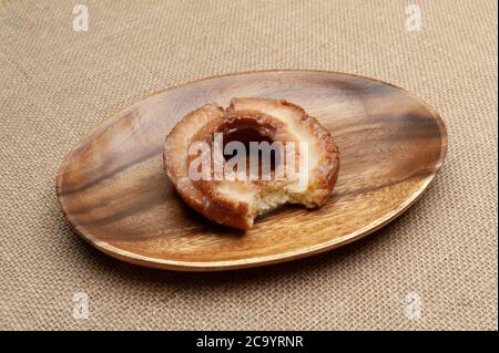 Deliziosa ciambella dolce morso su piatto di legno. Isolato su sfondo juto. Foto Stock