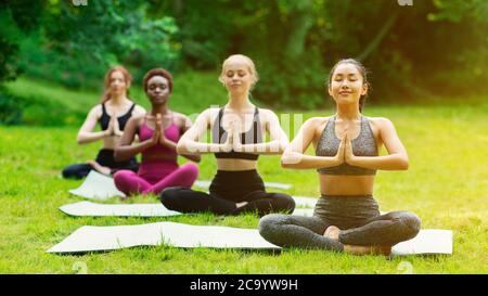 Ragazze diverse pacifiche meditating durante la loro pratica di yoga all'aperto in mattina Foto Stock