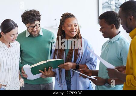 Ritratto in vita del team multi-etnico d'affari che ascolta la sorridente donna afroamericana durante la riunione in ufficio Foto Stock
