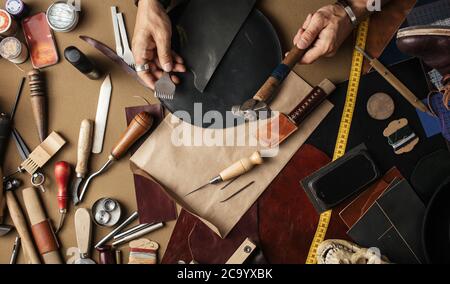 Close up di pelle designer mani rendendo custom made lavoro scarpe in vera pelle e un martello a un workshop. Foto Stock