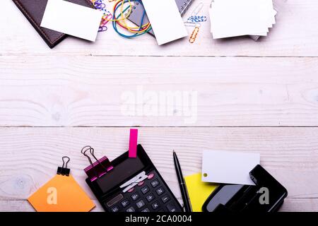 Carte vicino notebook, portafoglio, clip e penna su sfondo bianco di legno. Forniture per ufficio e concetto aziendale. Punzonatrice, elastici, perni e leganti vicino a note adesive gialle. Cancelleria e calcolatrice. Foto Stock