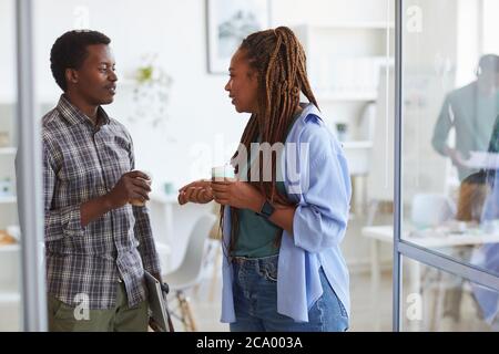 Vista laterale ritratto di una donna afroamericana contemporanea che parla con una giovane collega durante la pausa caffè in ufficio, copia spazio Foto Stock