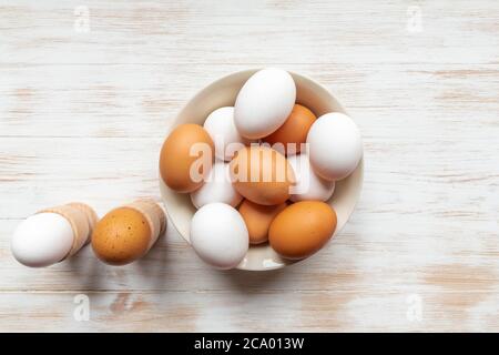 Uova marroni e bianche in ciotola su fondo di legno. Uova biologiche a gamma libera. Piatto con uova di pollo marroni e bianche, uova bollite in supporti sul tavolo Foto Stock