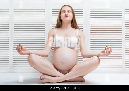 Bella giovane donna incinta meditando. Donna incinta facendo yoga a casa Foto Stock