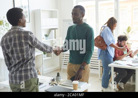 Ritratto di giovane afroamericano vestito in abito casual che scuote le mani con il collega attraverso il tavolo durante il primo giorno di nuovo lavoro, copia spazio Foto Stock