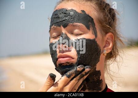 Giovane bella ragazza con una maschera di fango sulla sua faccia.la ragazza soffre di acne, una maschera di fango sulla sua faccia.Skin Care.Blue argilla. Foto Stock