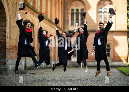 Cinque studenti di successo con congratulazioni insieme gettando cappelli di laurea in aria Foto Stock