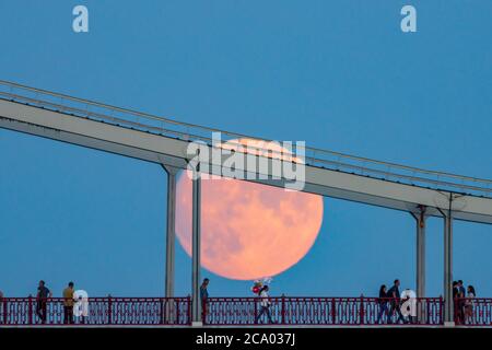 Sagome di persone sul ponte sullo sfondo della luna piena in aumento, Kiev, Ucraina Foto Stock