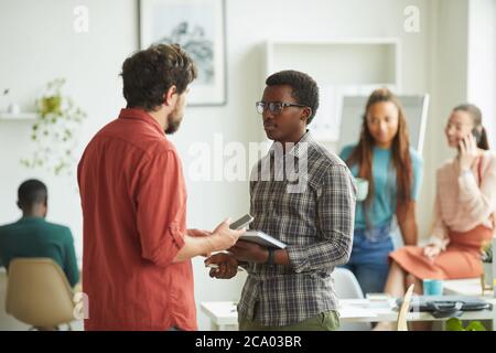 Vista laterale ritratto di manager agitato che istruisce il giovane afroamericano mentre si trova in ufficio, copia spazio Foto Stock