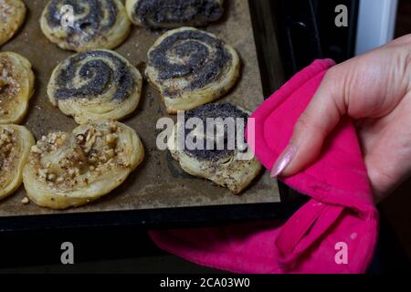 Una donna toglie i ricci cotti pieni di papavero e noci dal forno. Foto Stock