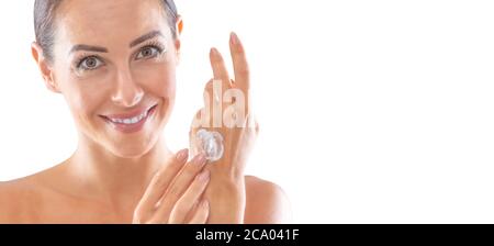 Bella giovane donna che applica crema alla sua mano isolata su bianco. Concetto di benessere e cosmetici per la cura della pelle. Foto Stock