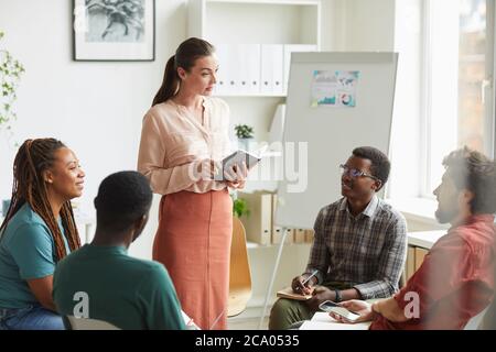 Gruppo multietnico di persone che siedono in cerchio mentre discutono la strategia per il progetto di business in ufficio, concentrarsi sul manager femminile dando istruzioni, spazio di copia Foto Stock