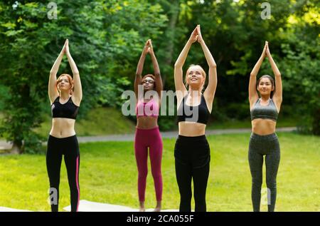 Belle ragazze multinazionali che fanno salutazioni sole yoga flusso al parco Foto Stock