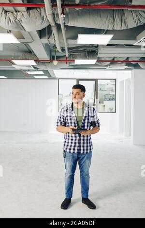 Report di ispezione dell'edificio per il riempimento di un giovane ingegnere serio durante il controllo delle linee di servizio nell'edificio in costruzione Foto Stock