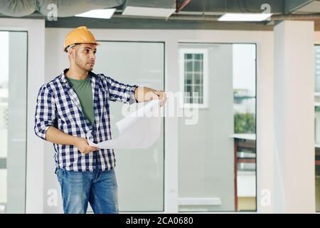 Serio bello giovane ingegnere di costruzione con linee di servizio di controllo di Blueprint in costruzione Foto Stock