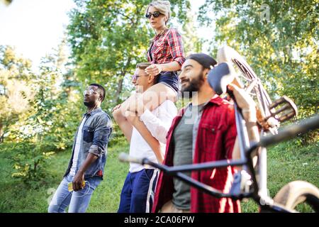 Felici adulti e ragazze in abbigliamento casual godendo di una lunga escursione a piedi al Giardino Botanico, donna felice è piggybacking su alto uomo biondo. Foto Stock