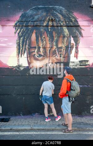 Due persone che dipingano su un murale di graffiti, di un giovane maschio nero con dreadlock, a Camden, Londra, Inghilterra Foto Stock