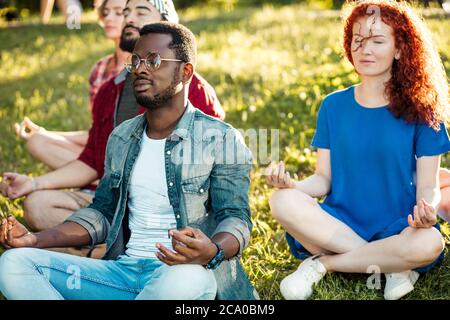 Gruppo di persone multietniche che si dialogano tra loro dopo essersi esercitate al parco. Coppie in una conversazione dopo una sessione di yoga all'aperto. Allegro gr Foto Stock