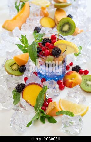 sete il bicchiere dissetante con acqua fredda e frutta fresca estiva con ghiaccio Foto Stock