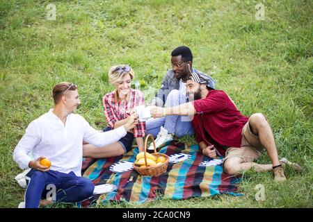 Gruppo di giovani simpatici colleghi che usano il tempo di pausa pranzo divertendosi all'aperto su green lownn, celebrando l'inizio di un nuovo progetto con bevande alla frutta Foto Stock