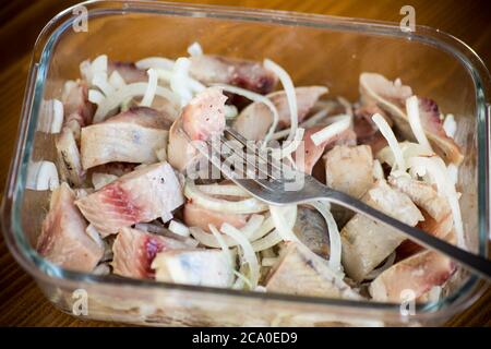 pezzi di aringhe salate fatte in casa con cipolle e spezie, su un tavolo di legno Foto Stock