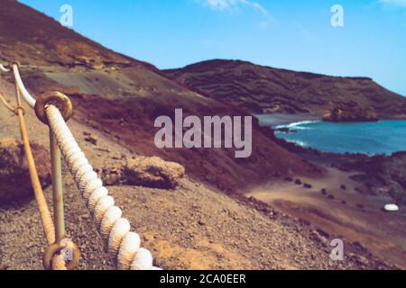 Corrimano di corda su una costa vulcanica rocciosa con terra rossa e sabbia nera sull'oceano Atlantico a El Golfo, Lanzarote, Isole Canarie, Spagna. Foto Stock