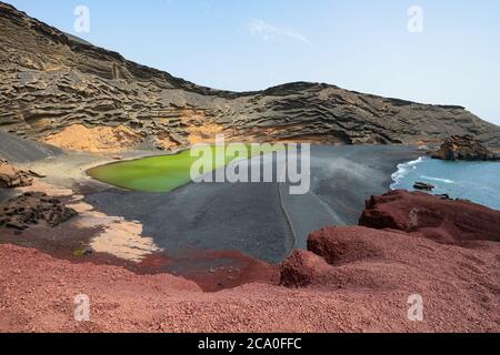 Lago Verde a El Golfo, Lanzarote, Isole Canarie, Spagna. Paesaggio colorato con spiaggia di sabbia nera, rocce vulcaniche scure e terra rossa. Foto Stock