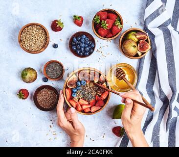 Vista dall'alto che mostra le mani di mangiare il porridge con miele, mirtilli e fragole su in legno di colore blu di sfondo tabella di buon mattino e sana prima colazione Foto Stock