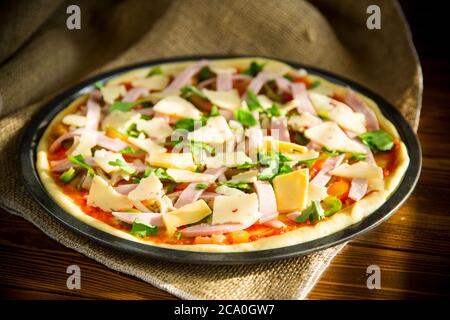 pizza cruda con ripieno assortito in metallo su un tavolo di legno Foto Stock