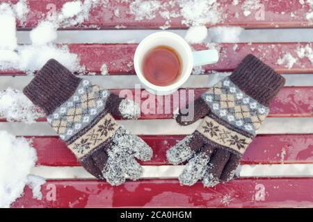 Tazza di tè e guanti in maglia da donna su una panca. Inverno, neve sotto. Vista dall'alto Foto Stock