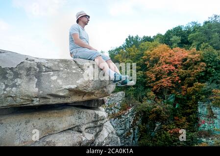 Un ragazzo si siede su una roccia in montagna su una pietra, vestito con una T-shirt e pantaloncini Foto Stock