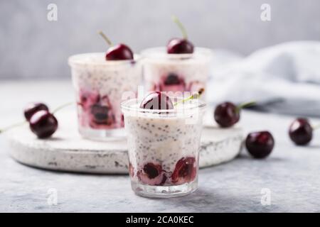 Budino di Chia con ciliegi, yogurt naturale, in un bicchiere su una superficie grigia. Messa a fuoco selettiva. Dessert sano, nutrizione adeguata, cibo super. Foto Stock
