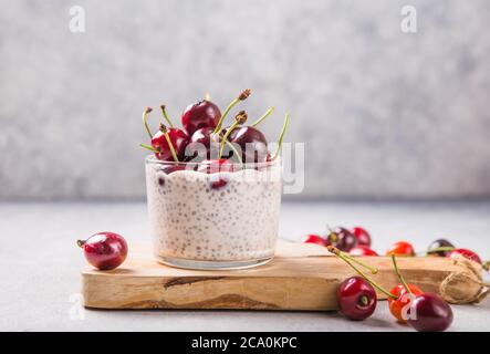 Budino di Chia con ciliegi, yogurt naturale, in un bicchiere su una superficie grigia. Messa a fuoco selettiva. Dessert sano, nutrizione adeguata, cibo super. Foto Stock