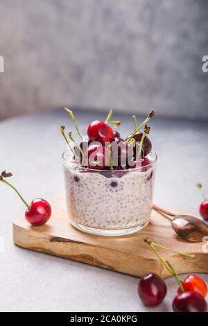 Budino di Chia con ciliegi, yogurt naturale, in un bicchiere su una superficie grigia. Messa a fuoco selettiva. Dessert sano, nutrizione adeguata, cibo super. Foto Stock