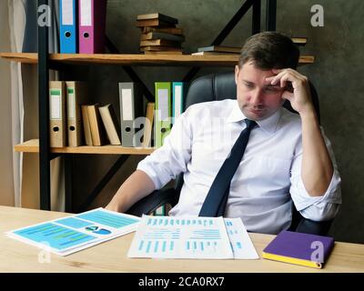 Un uomo d'affari stanco esamina la relazione finanziaria e i risultati dell'audit. Foto Stock