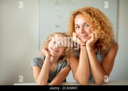 Niente potrebbe separarli o rompere questo amore. Ritratto emotivo di madre frizzy con capelli pelosi che abbracciava la sua adorabile figlia bionda riccia, sorridendo alla macchina fotografica Foto Stock