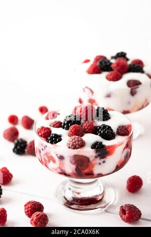 Deliziose bacche succose di lamponi e more con yogurt in forma di bicchiere su sfondo bianco Foto Stock