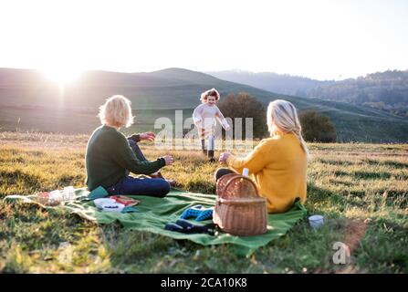 Bambina con madre e nonna che hanno pic-nic in natura al tramonto. Foto Stock