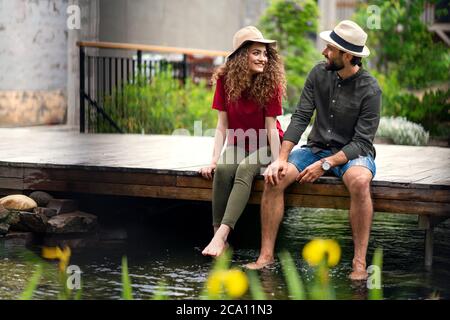 Giovane coppia che si siede all'aperto vicino all'hotel sul lago in vacanza, divertendosi. Foto Stock