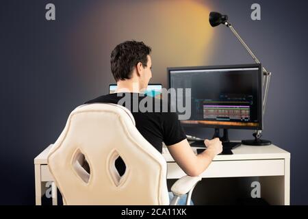 l'editor video freelance si siede su una sedia e una scrivania bianche nel suo ufficio e taglia alcuni video con un tablet grafico Foto Stock