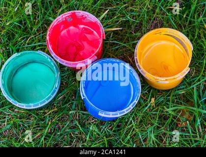Kit di quattro piccoli contenitori riempiti con diversi colori di vernice per dita sull'erba. Concetto di creatività, hobby artistico o divertimento di pittura Foto Stock