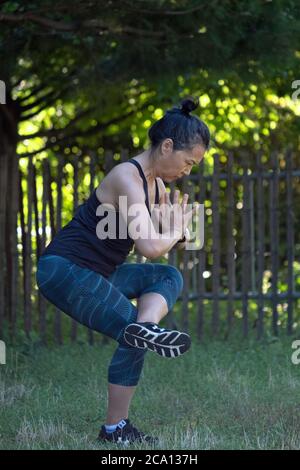 Una donna americana asiatica di mezza età adatta fa esercizi di yoga stretching da sola in un parco a Flushing, Queens, New York City Foto Stock